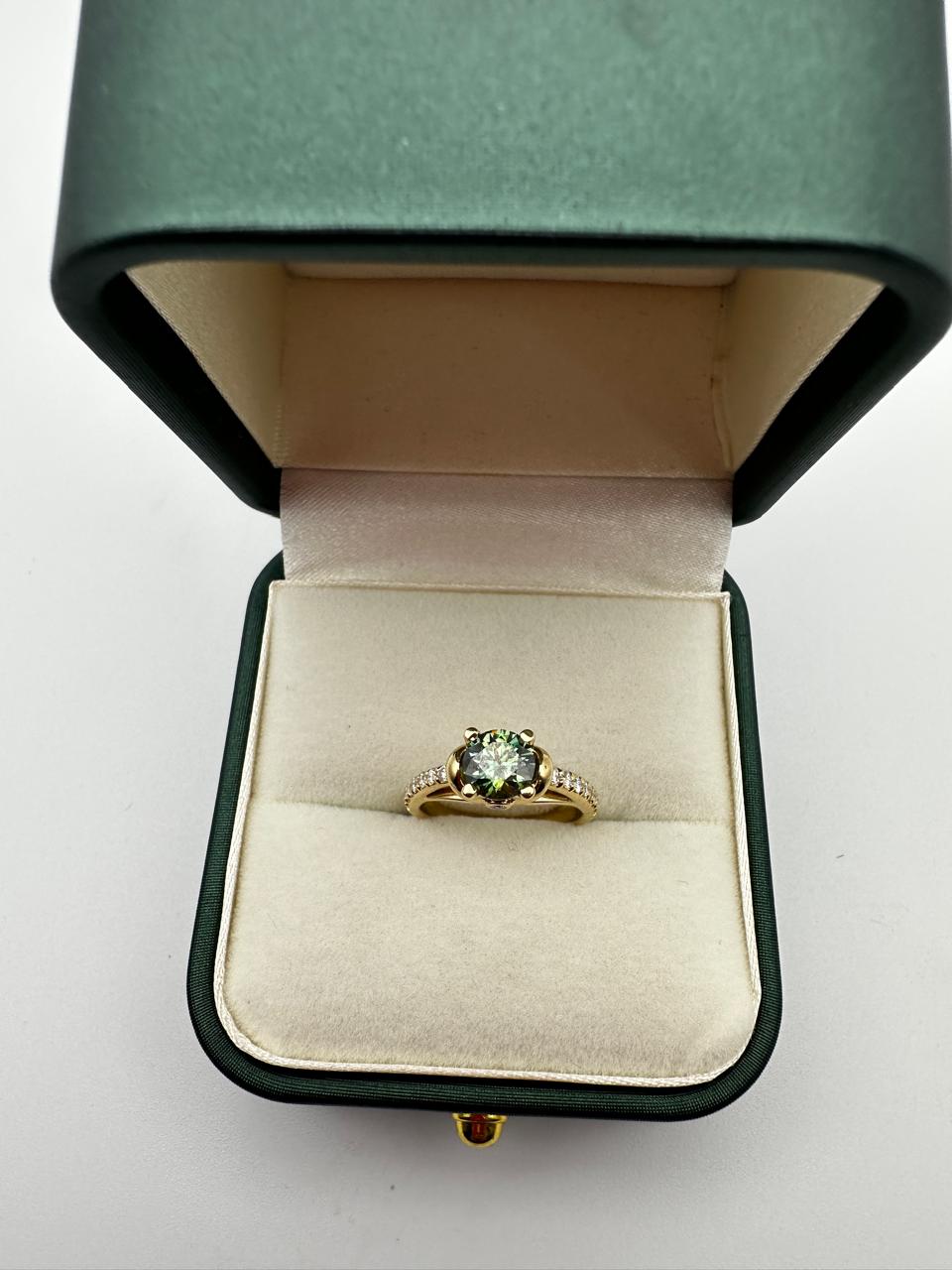 Gold ring with a green gemstone in a green velvet box on a white background